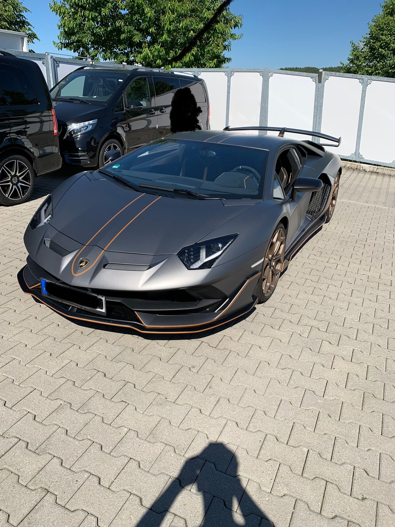 Grauer Lamborghini mit orangen Akzenten auf Parkplatz, Tageslicht, Hochformat