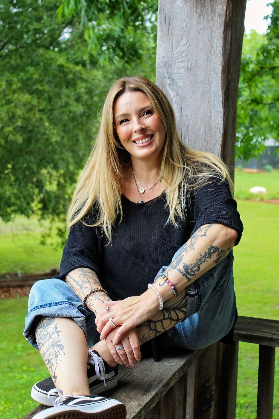 Smiling woman with tattoos sitting outdoors on a wooden fence.