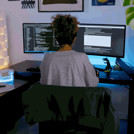 Animated GIF of woman doing the arm wave, sitting in front of 2 computer monitors