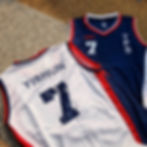 Two sports jerseys on textured ground. One navy, one white, both with "7." Navy shirt reads "YPS," white reads "YISHUN." Red details.