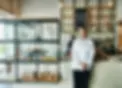 Bäckerin steht an der Theke in ihrem Bäckereigeschäft und begrüßt Gäste