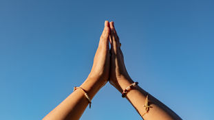 Hands joined in a gentle prayer position against a blue sky, symbolising balance, grounding and mindful Qigong posture.