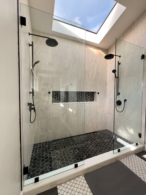 Close-up of a walk-in shower remodel in Serra Mesa featuring a skylight, frameless glass, hex tile floor, and modern black fixtures
