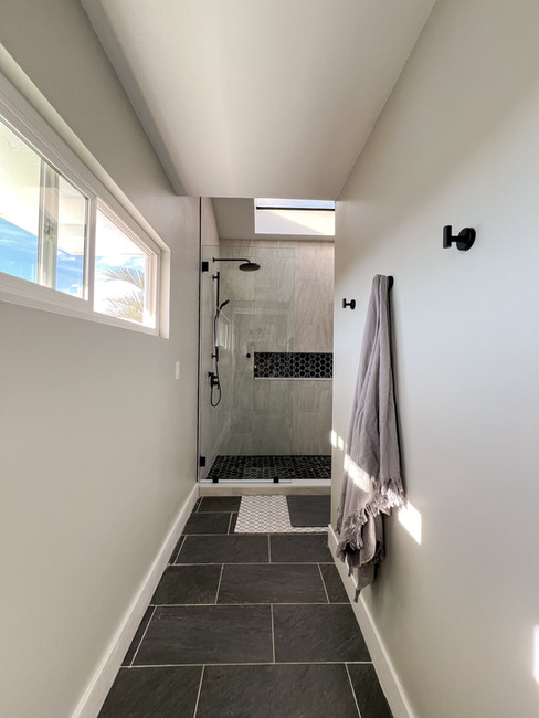 Bathroom remodel in Serra Mesa showing a hallway view toward a walk-in shower with skylight, modern tile flooring, and updated finishes.