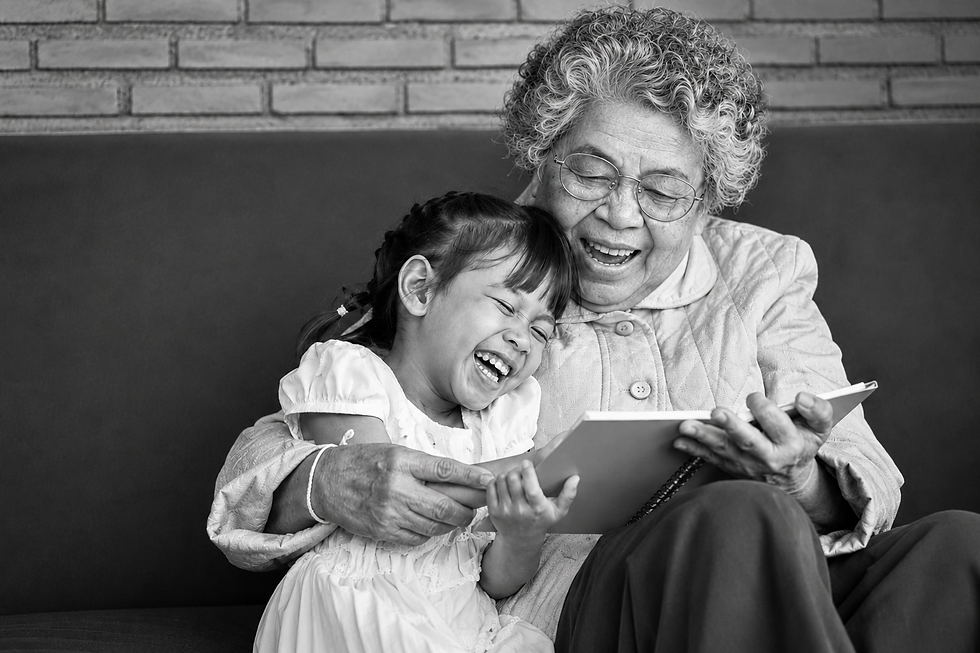 Black-and-white photo of a grandmother and young granddaughter laughing together while looking at a book, representing family