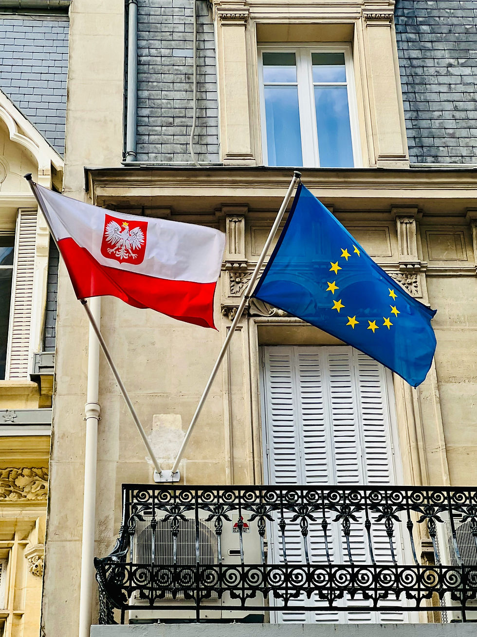 Polish and EU flags hang from a balcony on a historic building facade with shuttered windows.