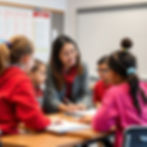 A teacher visits four students at their desks to teach them.