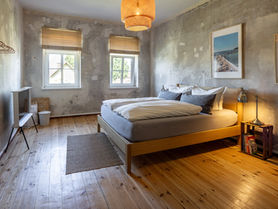 Schlafzimmer mit Doppelbett, Samsung Serife Fernseher, zwei Fenster mit Holzrollo und Nachttisch mit Nachttischlampe.