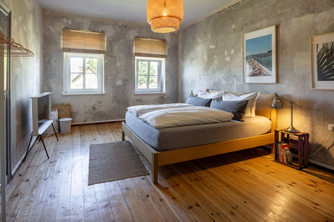 Schlafzimmer mit Doppelbett, Samsung Serife Fernseher, zwei Fenster mit Holzrollo und Nachttisch mit Nachttischlampe.