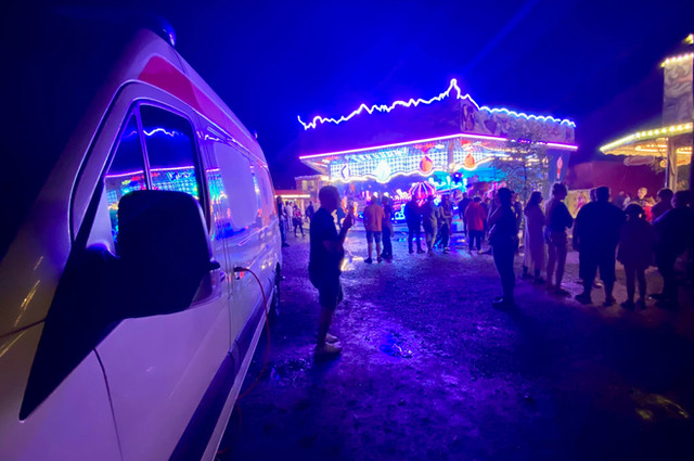 Beleuchteter Sanitätsdienst-Einsatz bei Nacht auf einem Jahrmarkt mit Fahrgeschäften und Besuchergruppen