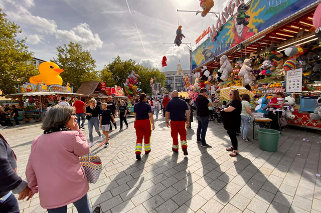 Einsatzkräfte der Rettungsdienstschule Rettungsanker® Bremen auf einem Stadtfest mit Kirmesständen und Besuchergruppen bei Sonnenschein