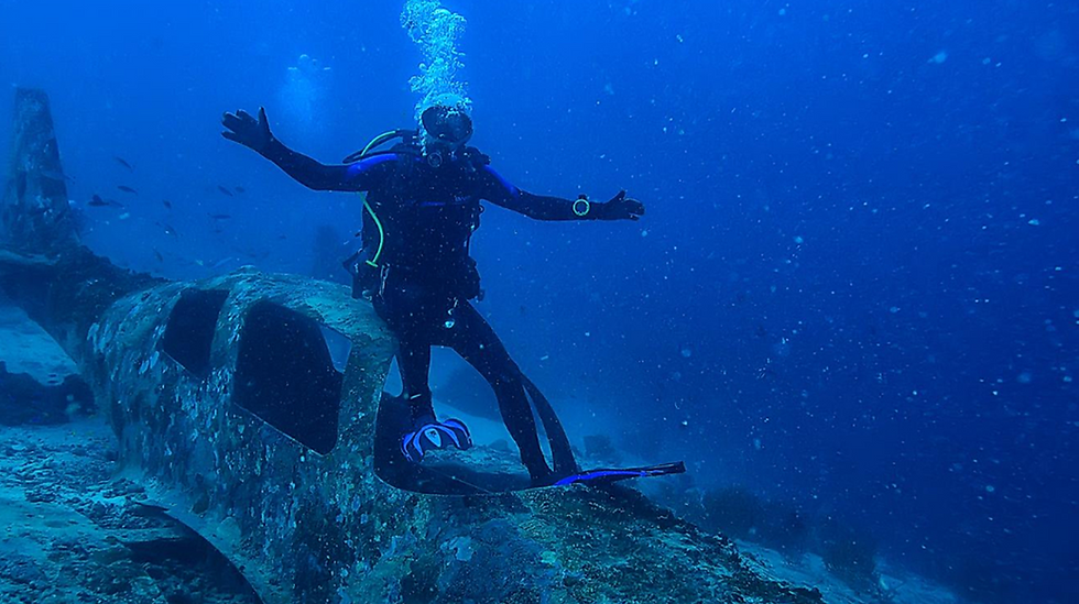 Taucher unter Wasser mit ausgebreiteten Armen über einem Wrackteil; Luftblasen steigen auf, blaues Meer und schwebende Partikel im Hintergrund – Symbolbild fürs Tauchen und Dekompressionsrisiko.