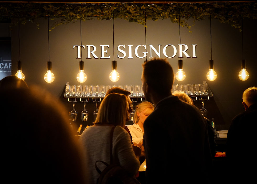 Beleuchtetes Schild 'TRE SIGNORI' über Gästen in einer Bar