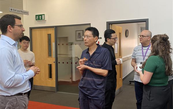 People standing and networking holding mugs. They are standing on a red rug; there are four men and one woman.