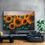 Thumbnail: An extra large vibrant landscape painting of sunflowers set in a beautiful lounge against a cementuous coloured wall.