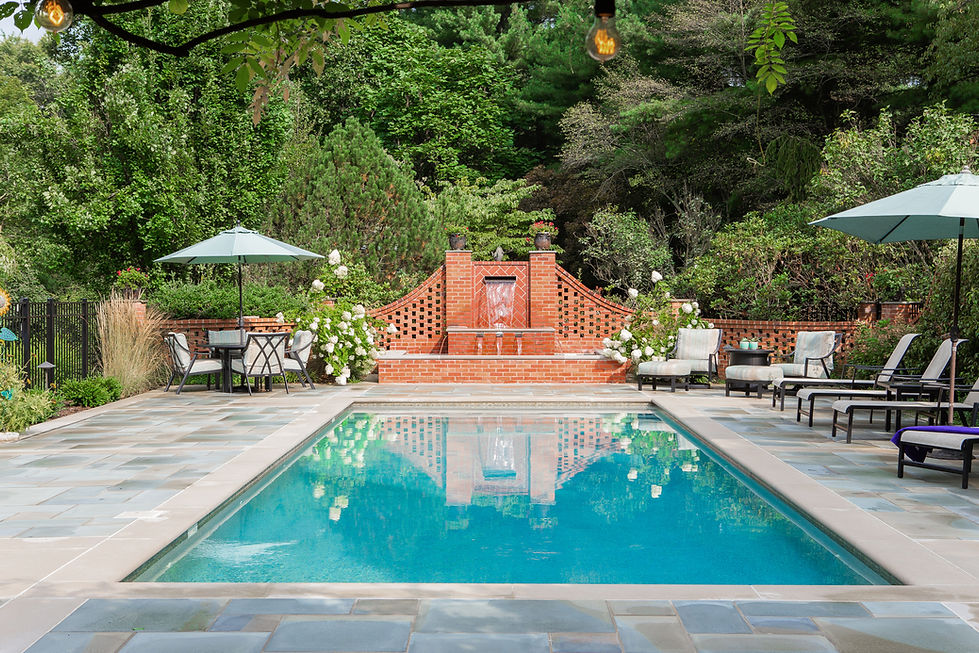 Swimming pool with brick fountain and lounge chairs.