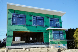 Front of the two-story home with green house wrap and new windows during framing