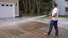 Power washing technician cleaning a residential concrete driveway with high-pressure spray