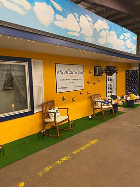 Entrance of the A Wish Come True facility with a yellow wall, a sign, and rocking chairs