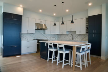 Kitchen with navy and white cabinets, pendant lights, and a large island with counter stools