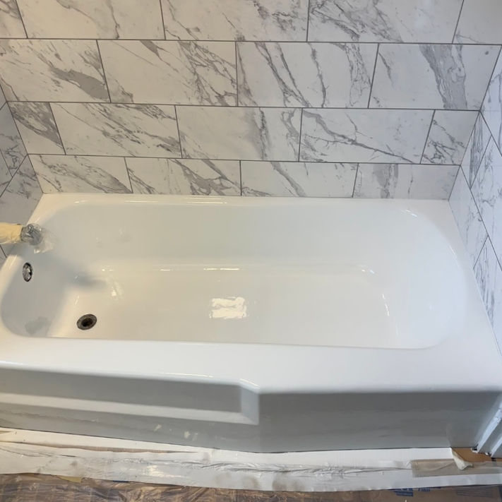 Refinished white bathtub with marble tile after reglazing