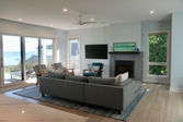 Living room with a gray sectional, fireplace, and wall-mounted TV beside windows facing the water