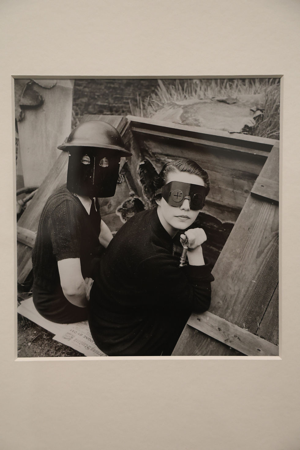 Kobiety w maskach przeciwogniowych, Downshire Hill, Londyn, 1941. Zdj. Lee Miller. Victoria and Albert Museum, Londyn. Dwie modelki siedzą w wejściu do schronu przeciwlotniczego w ogrodzie domu Lee Miller i Rolanda Penrose’a w Hampstead. Maski z kauczuku i ocynkowanej blachy noszono dla ochrony przeciwko bombom zapalającym.