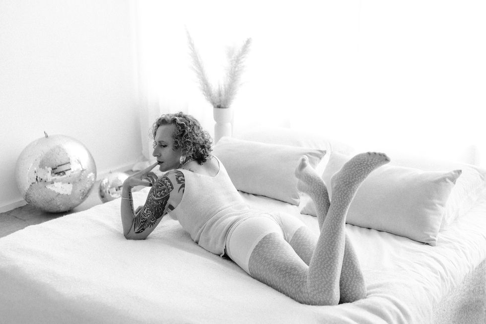 Transgender beauty model lounging on bed in high-key lighting, soft sensuality