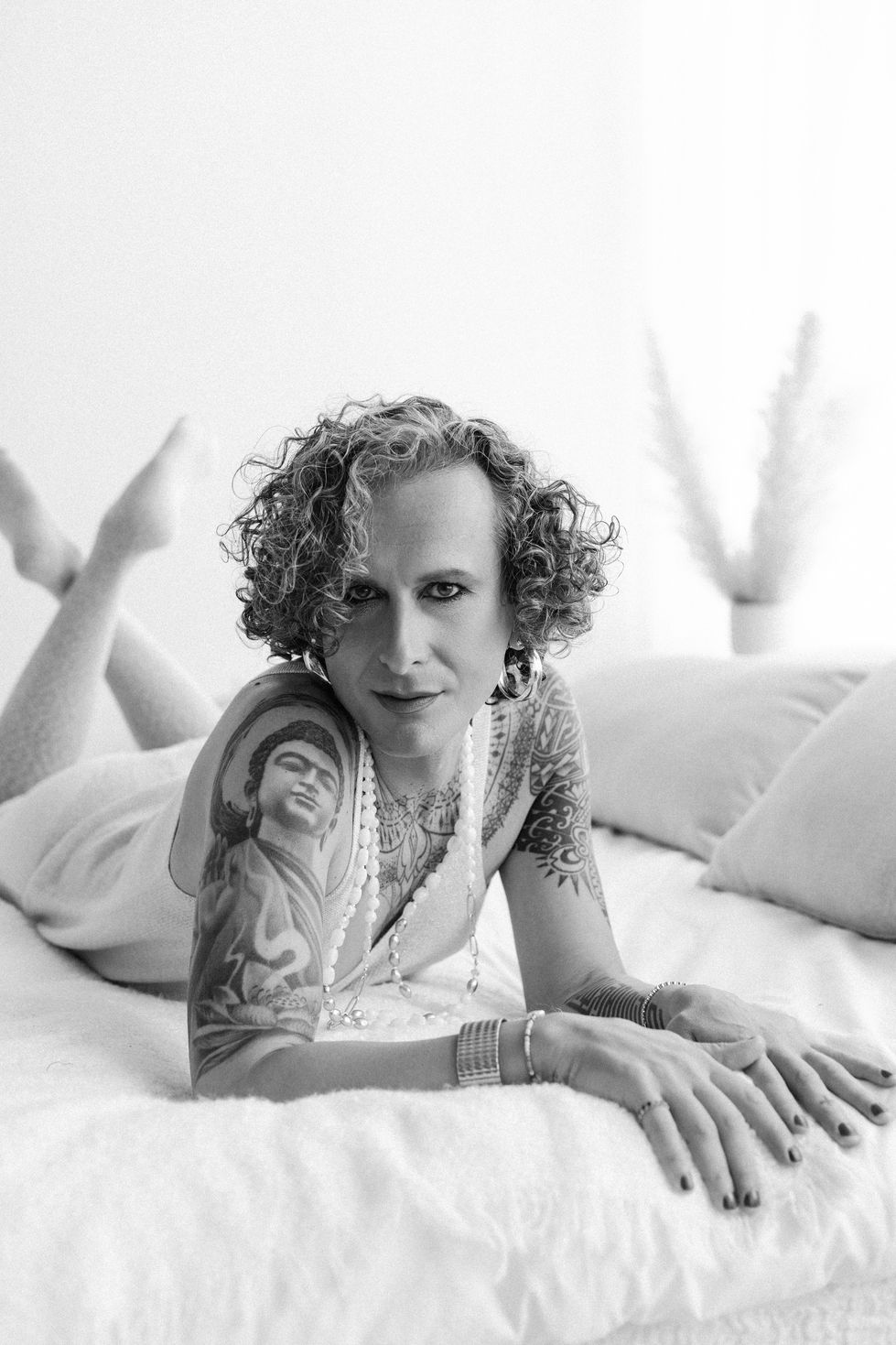 Relaxed editorial portrait of trans female model lying in soft bedding