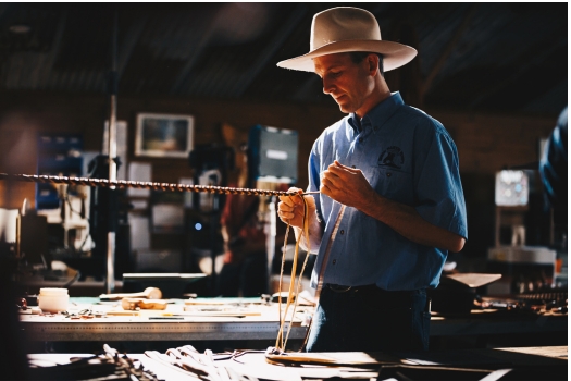 Man standing in his workshop braiding leather to make handcrafted whip.