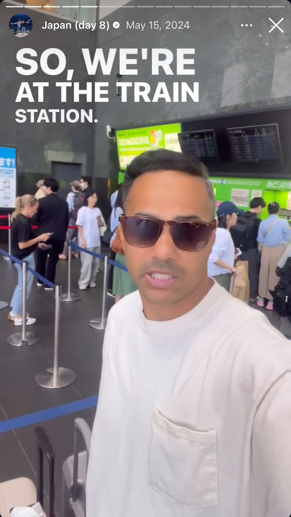 man wearing sunglasses standing by luggage at train station