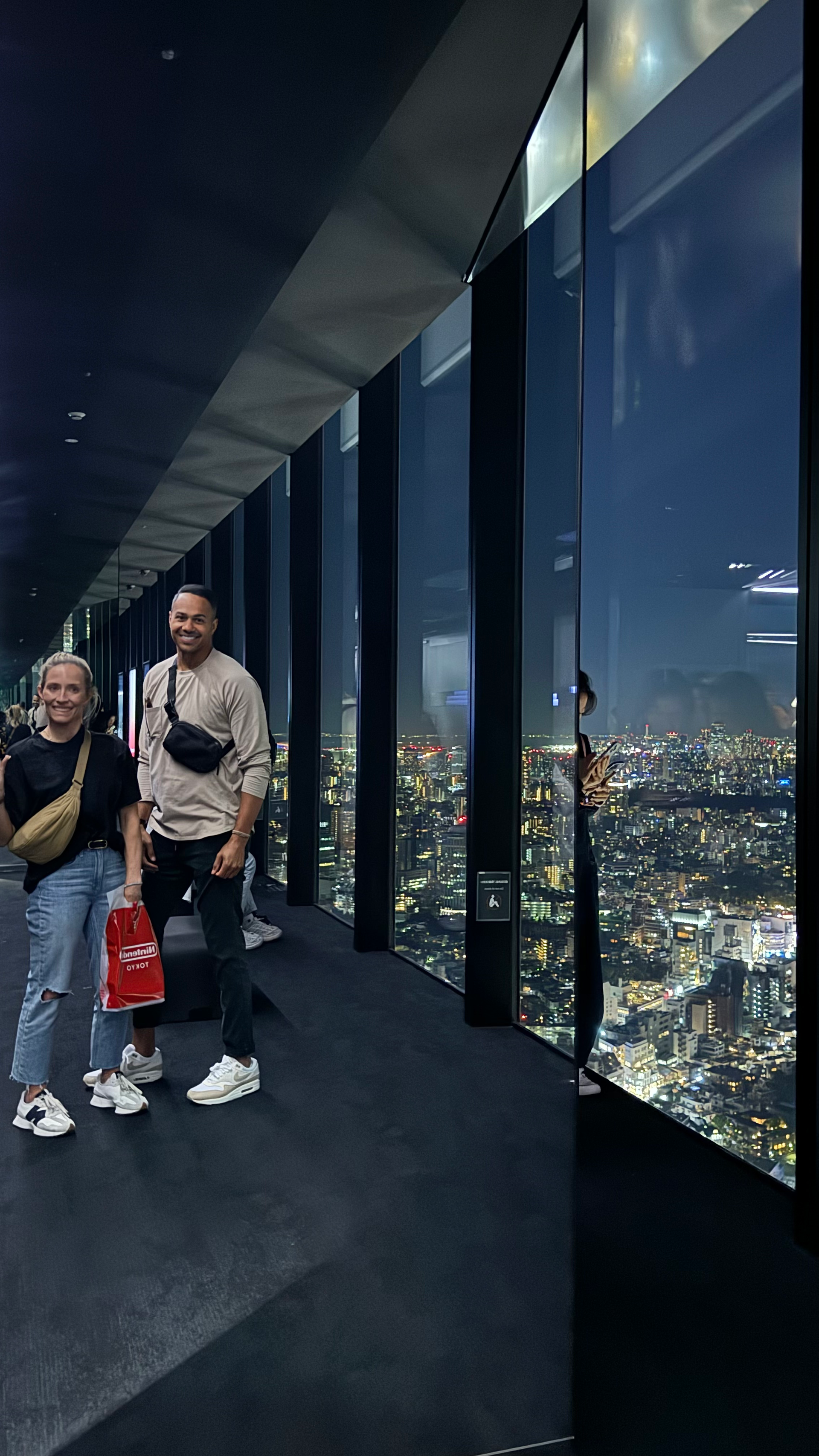 man and woman pose for picture by glass window of tall building in tokyo