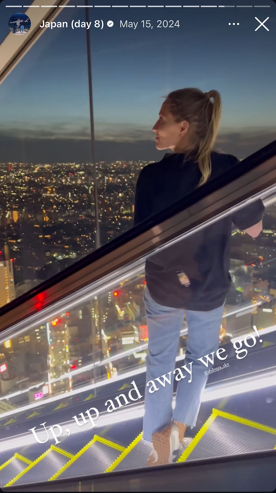 woman rides escalator with skyline in background