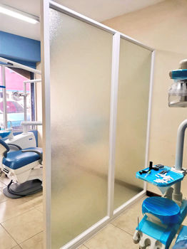 División fija fabricada en PVC blanco, con vidrio nevado; instalada para dividir dos espacios en una clínica dental.