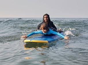 A kid is enjoying to learn surfing, he looks very happy as he is being pushed by the surfing instructor