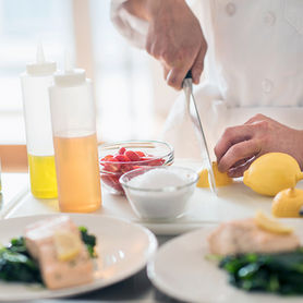Chef slicing a lemon for a plated salmon dinner.