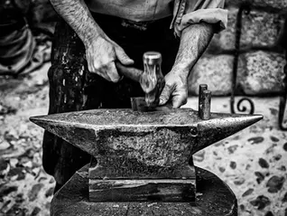 Black and white image of hands using a hammer on an anvil