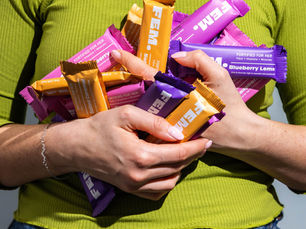 A women wearing a green top is holding lost of FEM health bars in her hands against her body. They look like they are going to fall out of her hands.
