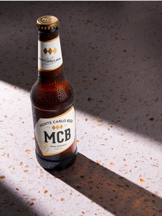 A bottle of Monte Carlo in a spotlight on a white and brown speccled surface. The spotlight is casting a harsh shadow of the bottle.