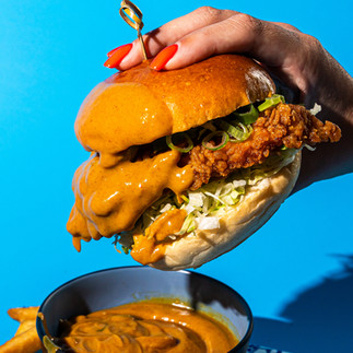 A hand hold a burger against a blue background, sauce drips off the side 