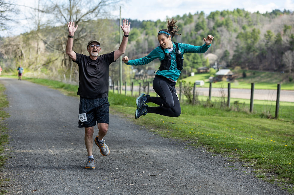 Father and adult daughter joyfully running and jumping on a rural path, lush green fields and trees in the background. Man wears race bib 584.