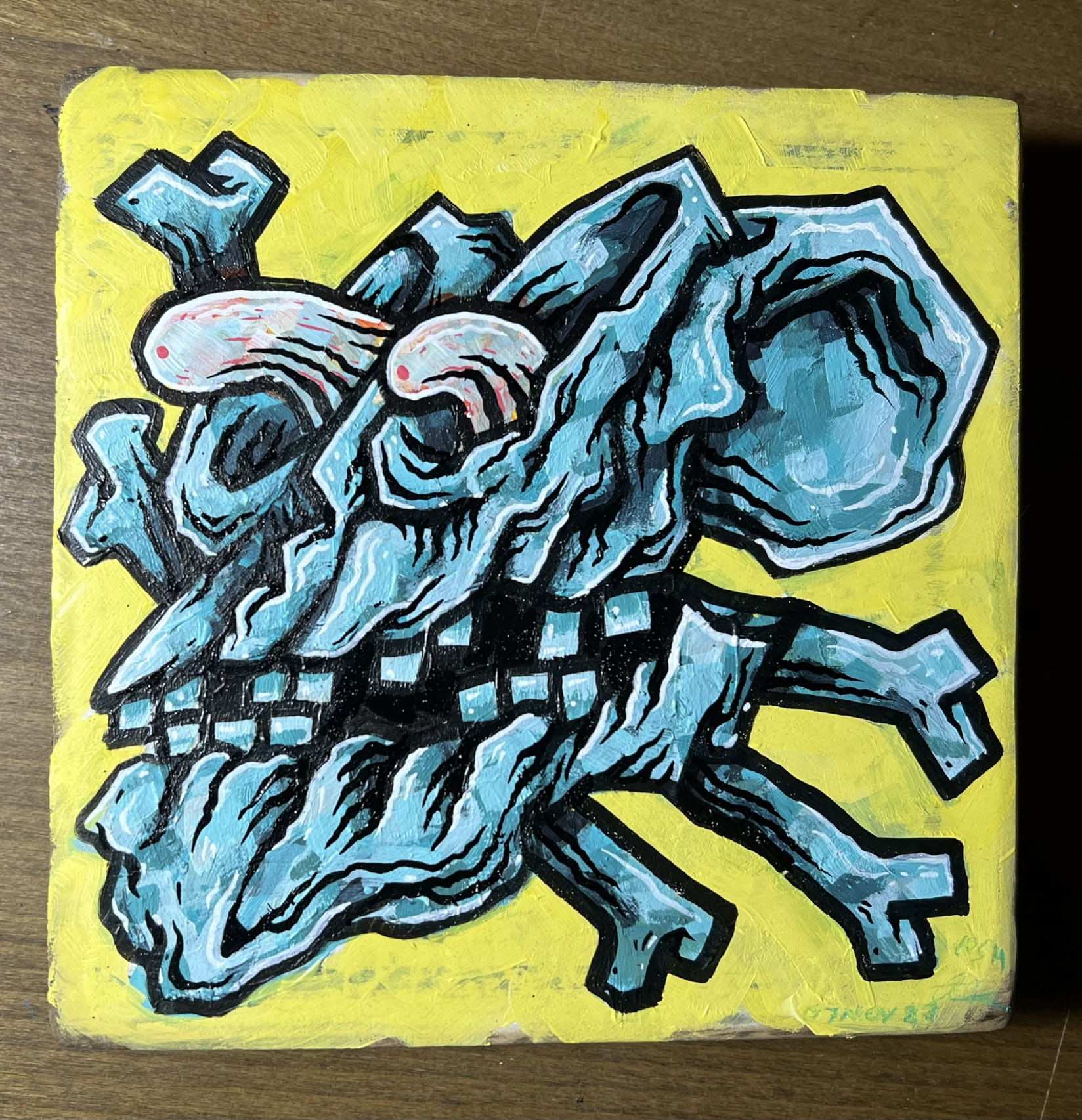 Acrylic painting of a blue skull on yellow wood with rat fink style eyeballs