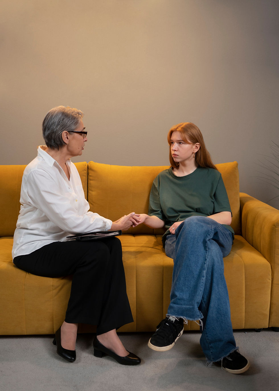 Woman and girl holding hands, having a seated conversation on a couch.