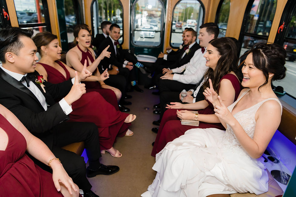 Wedding party riding on a trolley, dressed in formal attire, laughing and playing a game with hand gestures.
