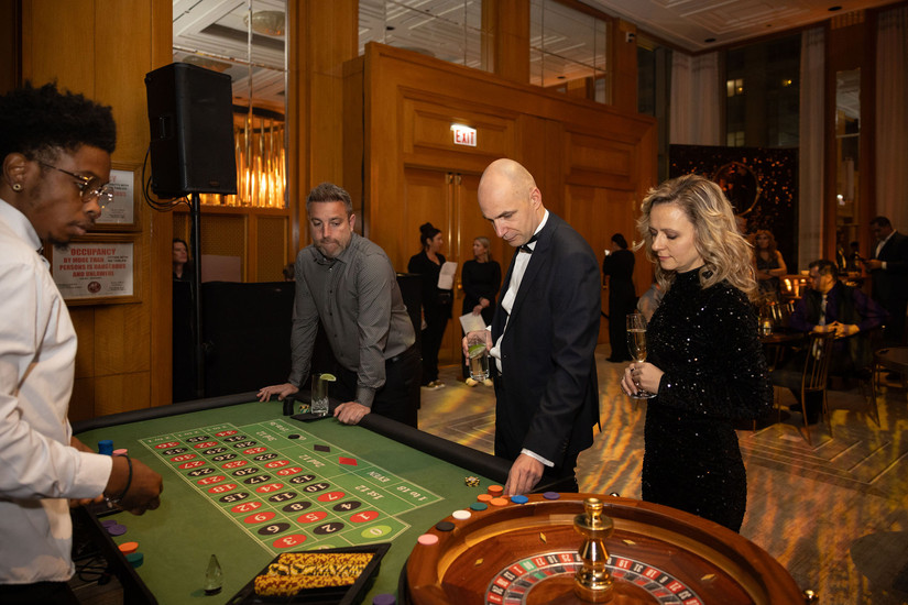 Guests in tuxedo and formal attire placing bets at a roulette table with a professional dealer at an upscale Chicago casino event