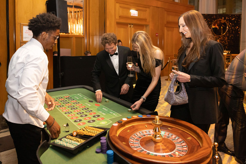 Group of guests smiling and placing chips on a roulette table with a professional dealer at a formal Chicago casino night event