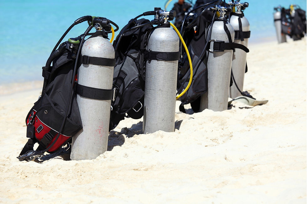 Scuba tanks with gear stand upright on sandy beach, with crystal blue sea in the background. Bright sunlight creates a warm, inviting scene.