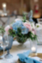 Elegant table setting with pastel flowers in a vase, blue napkins, a lit candle, and blue glassware. Soft, romantic ambiance.