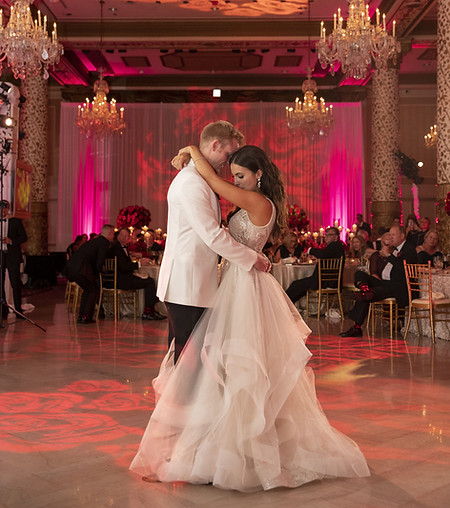 Bride and groom sharing their first dance in a grand ballroom with pink uplighting and chandeliers