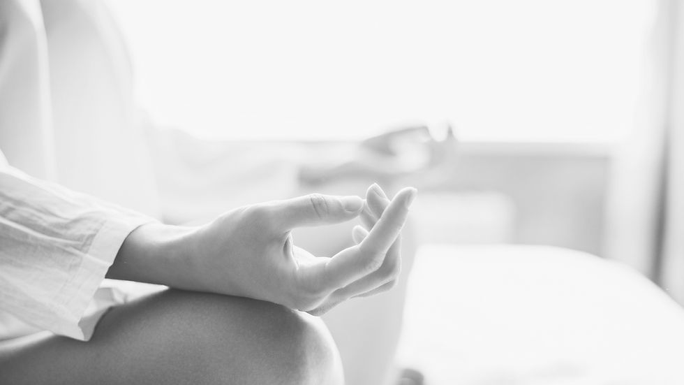 Eine Frau sitzt meditierend in Stille, ihre Hände in einer Mudra-Haltung, eingefangen in einem stimmungsvollen Schwarz-Weiß-Bild.